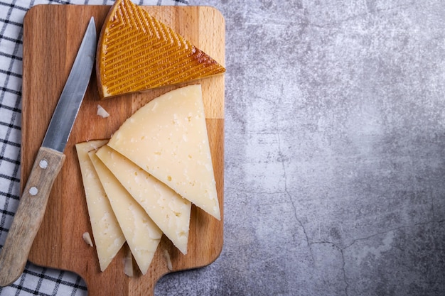 Vista superior de trozos triangulares de queso manchego curado y un cuchillo afilado en una tabla de comida de madera