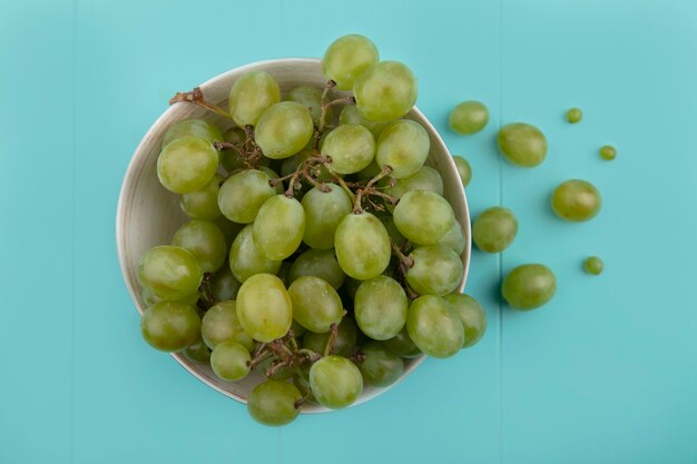 Vista superior de la uva blanca en un tazón y sobre fondo azul.