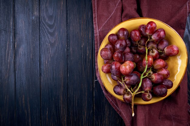 Vista superior de uva dulce fresca en un plato sobre la mesa de madera oscura con espacio de copia