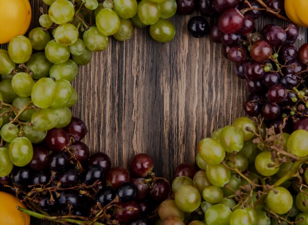 Vista superior de uvas blancas y negras con albaricoques sobre fondo de madera con espacio de copia