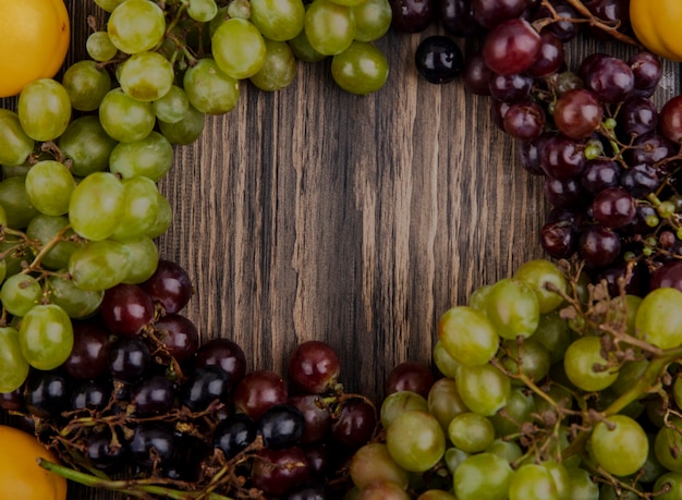 Vista superior de uvas blancas y negras con albaricoques sobre fondo de madera con espacio de copia