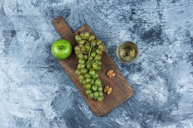 Vista superior de uvas blancas, nueces, manzana en tabla de cortar con vaso de whisky sobre fondo de mármol azul oscuro. horizontal