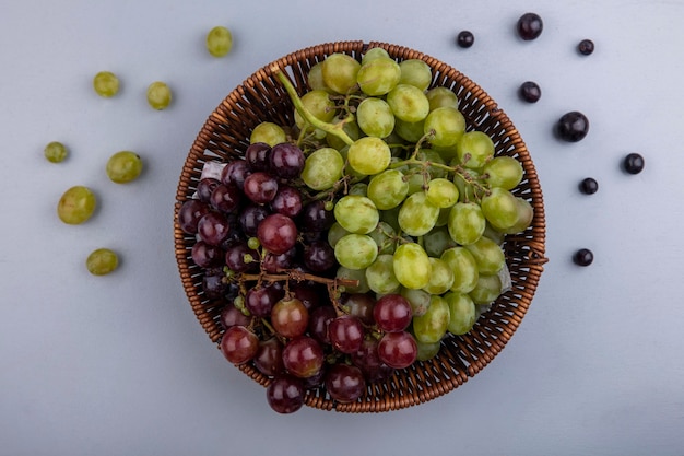 Vista superior de uvas en canasta y patrón de bayas de uva sobre fondo gris