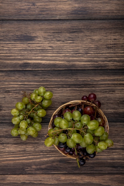 Vista superior de uvas en canasta y sobre fondo de madera con espacio de copia