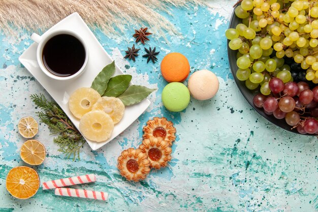 Vista superior de uvas de colores frescos con una taza de té macarons y galletas en la superficie azul claro frutas galleta azúcar dulce pastel hornear pastel