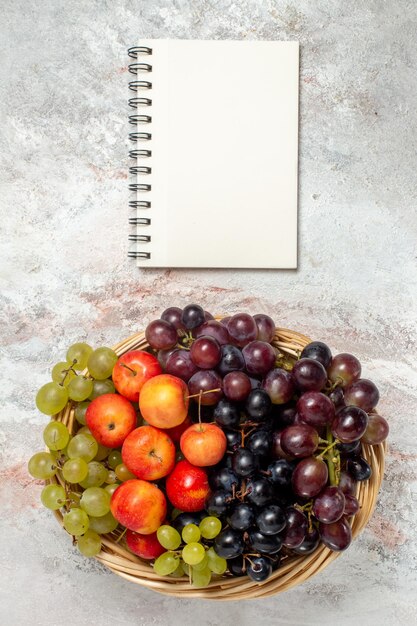 Vista superior de uvas frescas con ciruelas sobre superficie blanca