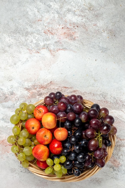 Vista superior de uvas frescas con ciruelas sobre superficie blanca