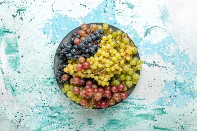 Vista superior de uvas frescas de color fruta jugosa y suave en el fondo azul claro, fruta, baya, jugo fresco y suave vino