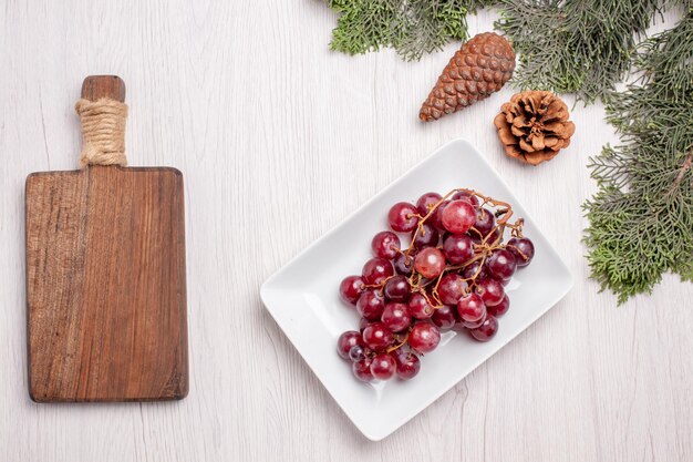 Vista superior de uvas frescas dentro de placa con árbol en mesa de madera