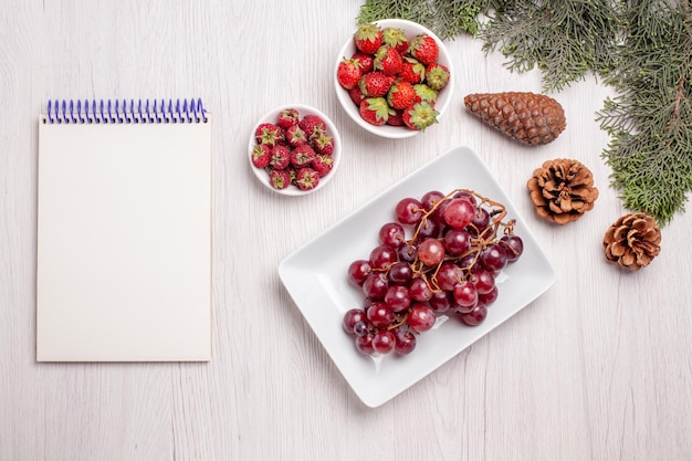 Vista superior de uvas frescas con fresas y frambuesas en mesa blanca