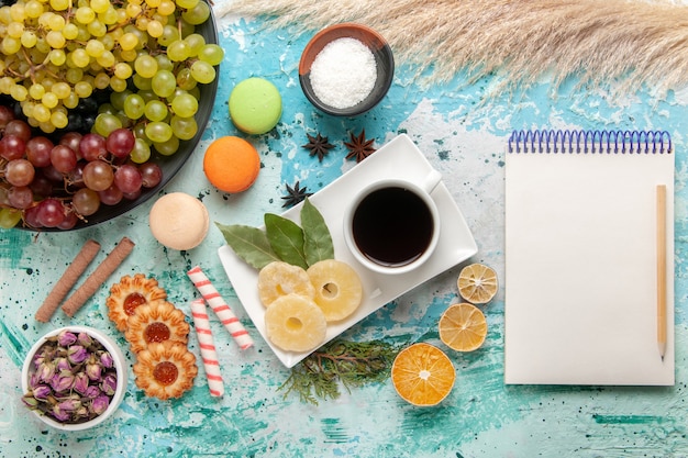 Foto gratuita vista superior de uvas frescas con galletas macarons franceses y una taza de té en el escritorio azul claro galletas galletas azúcar dulce té de la torta