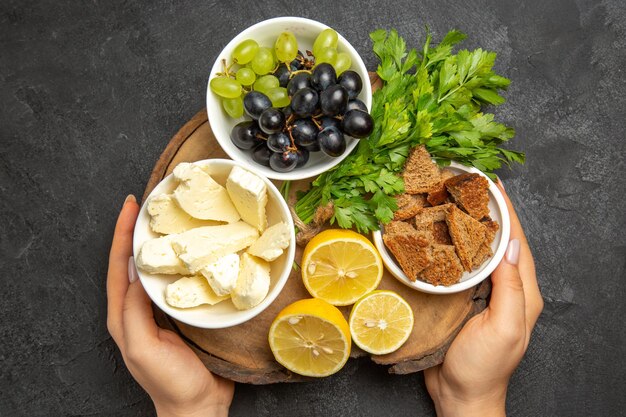 Vista superior de uvas frescas con queso blanco rodajas de limón y verduras en la superficie oscura comida comida leche fruta