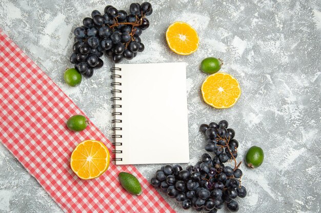 Vista superior de uvas negras frescas con bloc de notas de feijoa y naranjas en superficie blanca fruta madura fresca suave