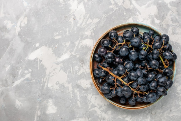 Vista superior de uvas negras frescas jugosas frutas dulces suaves en el escritorio blanco claro