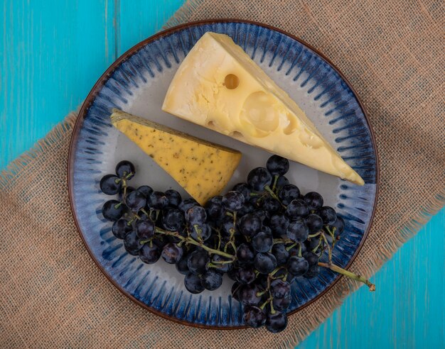 Vista superior de uvas negras con rodajas de queso en un plato sobre una servilleta beige