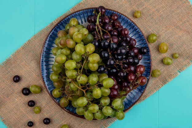Vista superior de las uvas en un plato con uvas en cilicio sobre fondo azul.