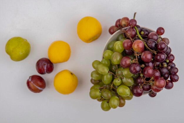 Vista superior de las uvas en un recipiente con pluots y nectacots sobre fondo blanco.