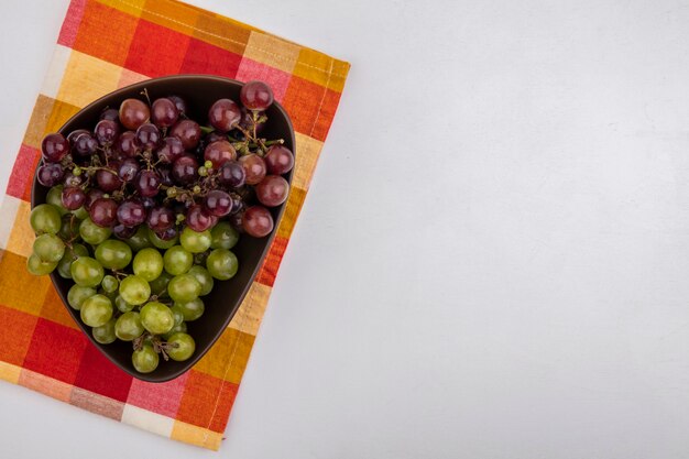 Vista superior de las uvas en un recipiente sobre tela escocesa sobre fondo blanco con espacio de copia