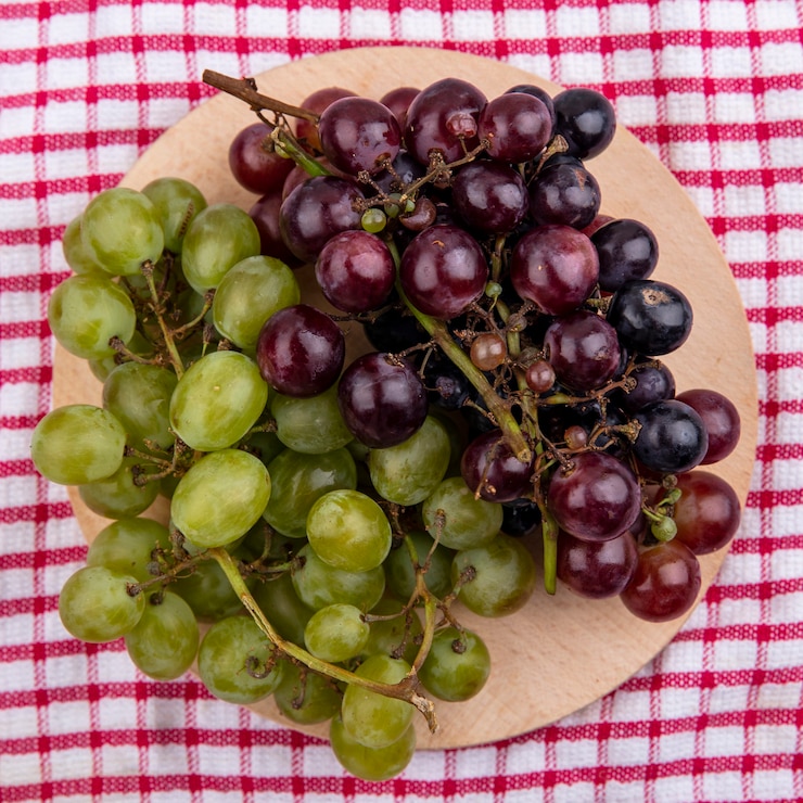 Foto gratuito vista superior de las uvas en la tabla de cortar sobre fondo de tela a cuadros
