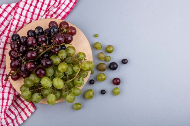 Vista superior de las uvas en la tabla de cortar sobre tela a cuadros y fondo gris con espacio de copia