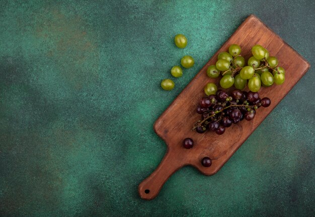 Vista superior de las uvas en la tabla de cortar con uvas sobre fondo verde con espacio de copia