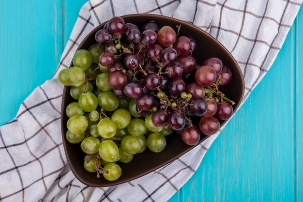 Foto gratuita vista superior de uvas en un tazón sobre tela escocesa sobre fondo azul.