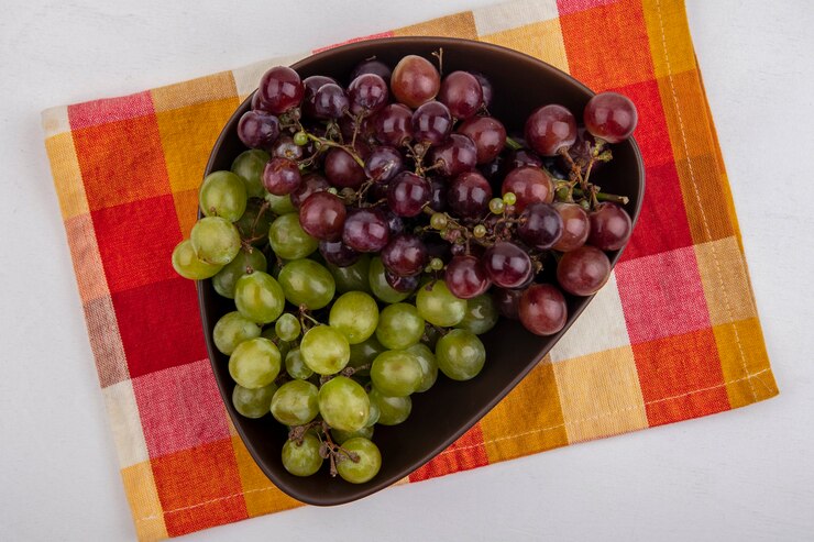 Foto gratuito vista superior de uvas en un tazón sobre tela escocesa sobre fondo blanco.