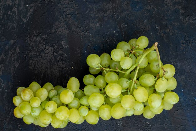 Una vista superior de uvas verdes frescas agrias, jugosas y suaves sobre el fondo oscuro, fruta madura, planta verde