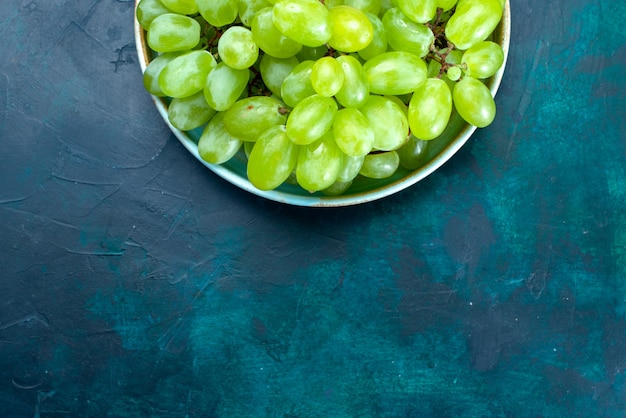 Vista superior de uvas verdes frescas frutas suaves y jugosas dentro de la placa en el escritorio azul oscuro.