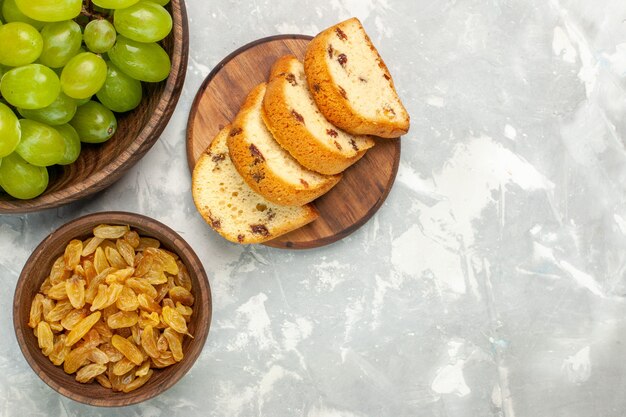 Vista superior de uvas verdes frescas suaves y deliciosas con tortas en un escritorio blanco claro