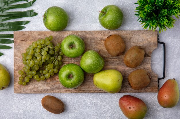 Vista superior de uvas verdes con manzanas verdes y kiwi en un soporte con peras sobre un fondo blanco.