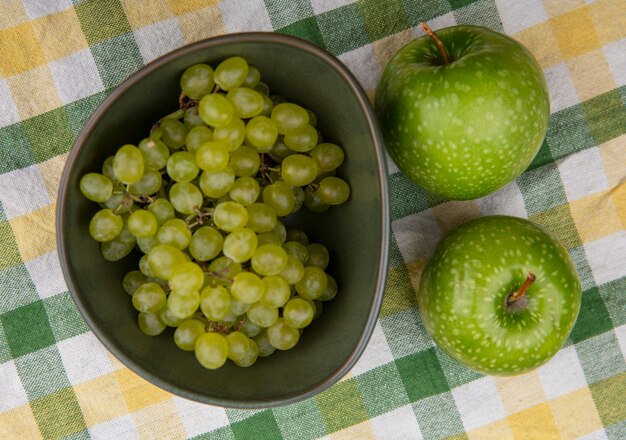 Vista superior de uvas verdes con manzanas verdes en una toalla a cuadros de color verde amarillo