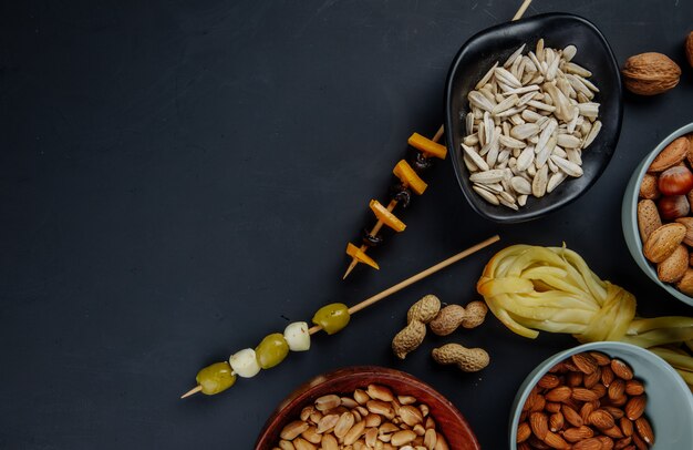 Vista superior de variados aperitivos de cerveza semillas de girasol maní almendras aceitunas en vinagre y queso en cadena en negro con espacio de copia