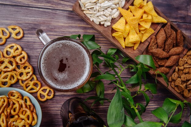 Vista superior de variados aperitivos de cerveza, semillas de girasol, papas fritas, galletas saladas y mini pretzels con una jarra de cerveza en rústica