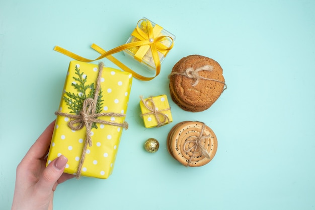 Vista superior de varias deliciosas galletas apiladas y mano que sostiene la caja de regalo amarilla sobre fondo verde pastel