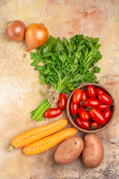 Vista superior de varias verduras frescas, como tomates roma, patatas, cebollas, zanahoria y un manojo de perejil para ensalada casera sobre un fondo de madera con espacio de copia