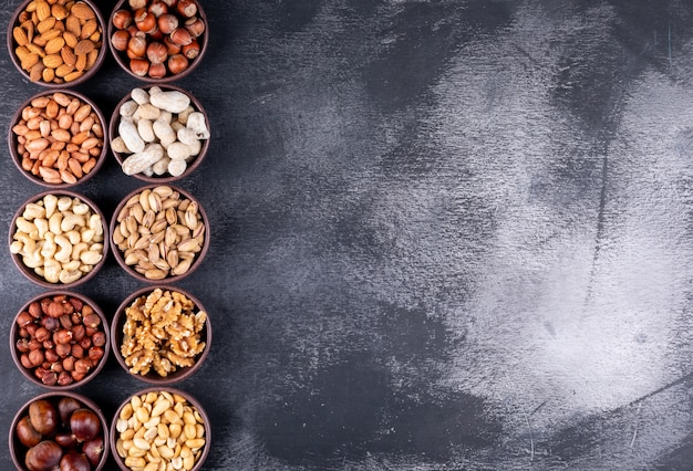 Vista superior de una variedad de nueces y frutas secas en mini tazones diferentes con nueces, pistachos, almendras, maní