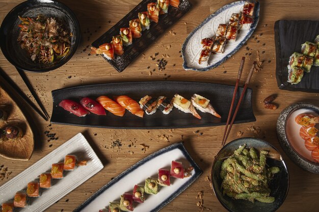 Vista superior de una variedad de sushi, nigiri, sashimi, yakisoba y edamame en una mesa de madera de restaurante