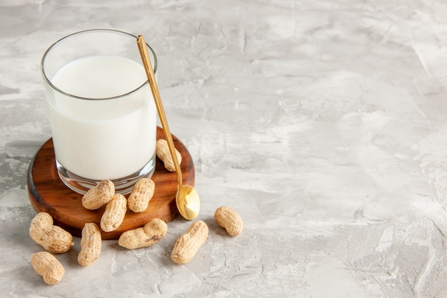 Vista superior del vaso lleno de leche en bandeja de madera y cuchara de frutos secos en el lado derecho sobre fondo blanco.