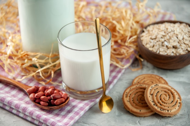 Vista superior del vaso de vidrio abierto lleno de leche y frijoles en una cuchara, galletas, avena en una toalla despojada de color púrpura