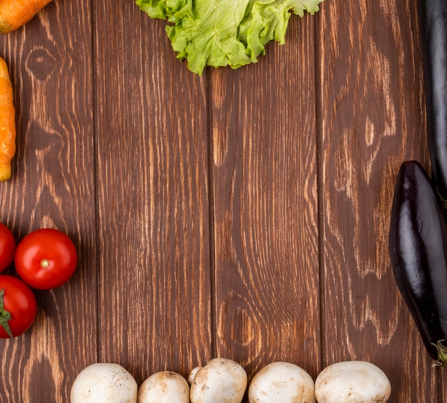 Vista superior de vegetales dispuestos como un marco berenjenas zanahorias tomates y champiñones sobre fondo rústico de madera con espacio de copia