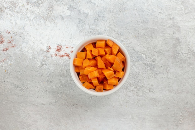 Vista superior de vegetales de naranja en rodajas dentro de una olla pequeña sobre fondo blanco.