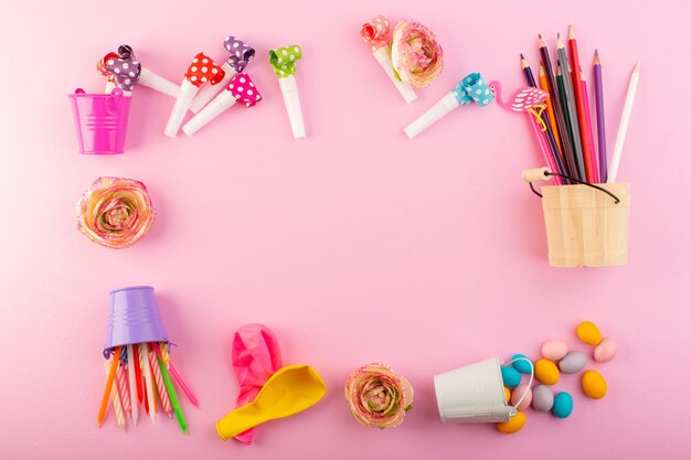 Una vista superior de velas y lápices junto con bolas y caramelos por toda la decoración de escritorio rosa, dulces de fotos en color