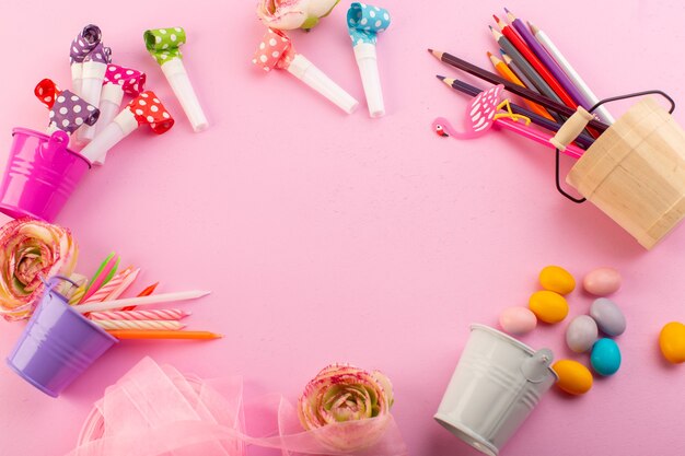 Una vista superior de velas y lápices junto con flores y dulces en el escritorio rosa decoración en color de cumpleaños.