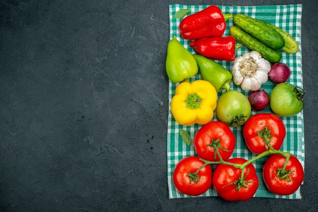 Vista superior verduras ajo pepinos cebolla roja tomate rama pimientos sobre mantel verde sobre mesa negra