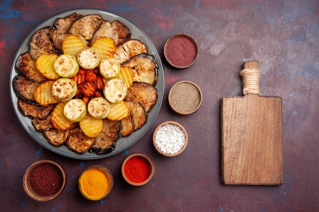 Vista superior de verduras al horno patatas y berenjenas con condimentos en el espacio oscuro