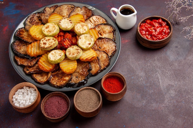 Vista superior de verduras al horno patatas y berenjenas con diferentes condimentos en el espacio oscuro