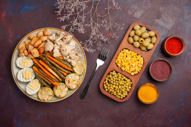 Vista superior de verduras cocidas con diferentes condimentos en el espacio oscuro