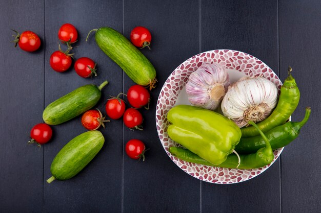 Vista superior de verduras como ajo pimienta en plato con tomates y pepinos en superficie negra