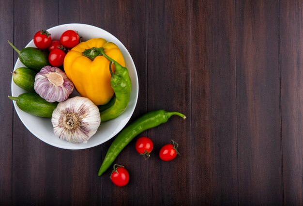 Vista superior de verduras como ajo pimiento pepino y tomate en un tazón sobre superficie de madera